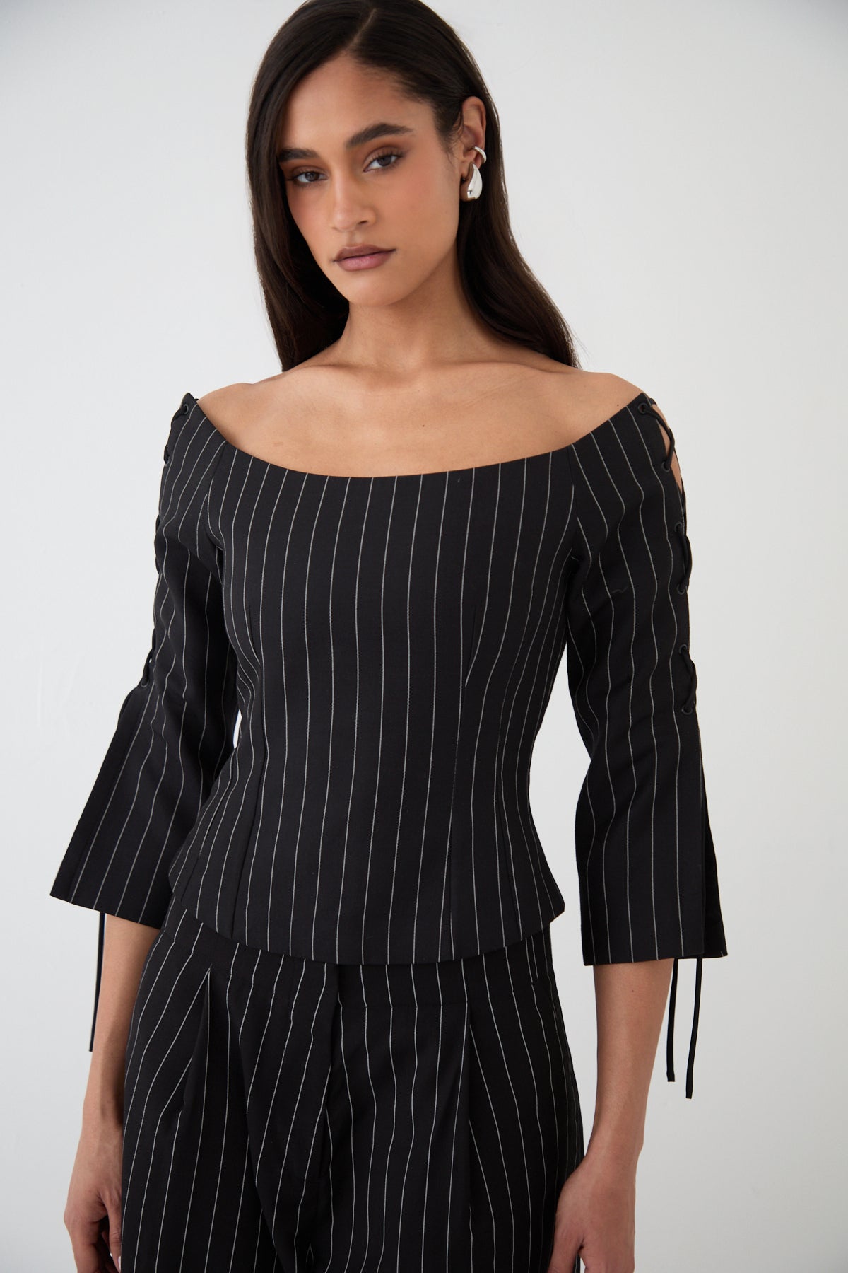 A model wearing a black pinstripe top with wide scoop neckline, lace-up 3/4 length sleeves.