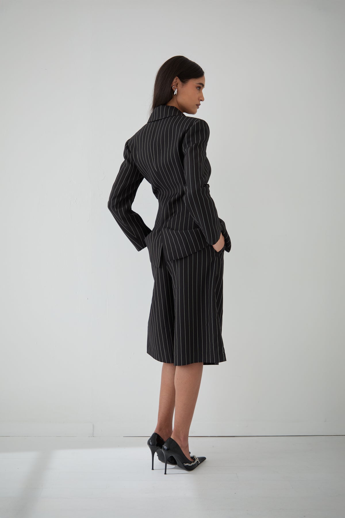A woman wearing a black pinstripe cinched blazer paired with matching pinstripe shorts.