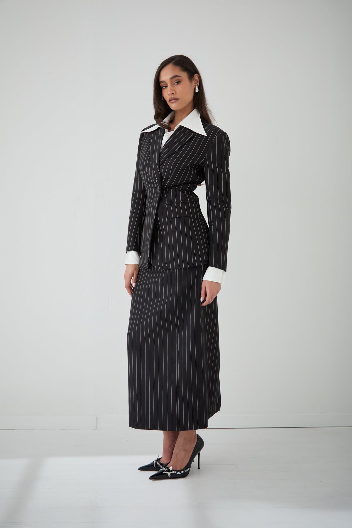 A woman wearing a black pinstripe cinched blazer paired with a white shirt and a matching pinstripe long skirt.