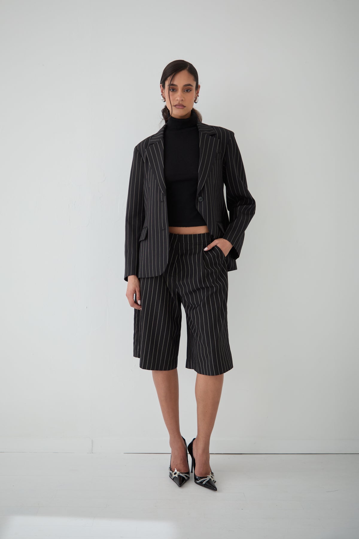 A woman wearing a pinstripe blazer  paired with a black turtleneck and matching pinstripe shorts.