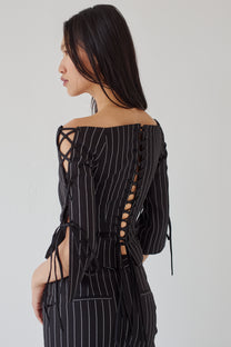 Woman wearing a black pinstripe outfit with lace-up details on a white background