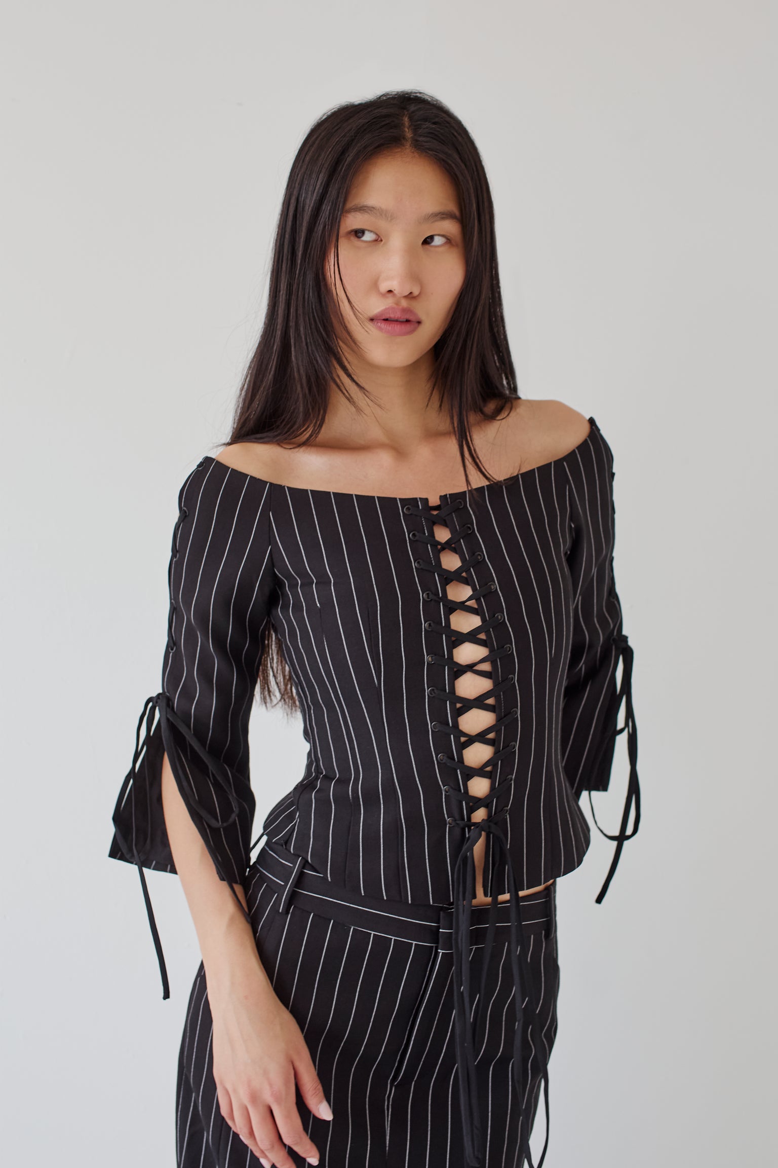 Woman wearing a black pinstripe outfit with a lace-up front on a plain background