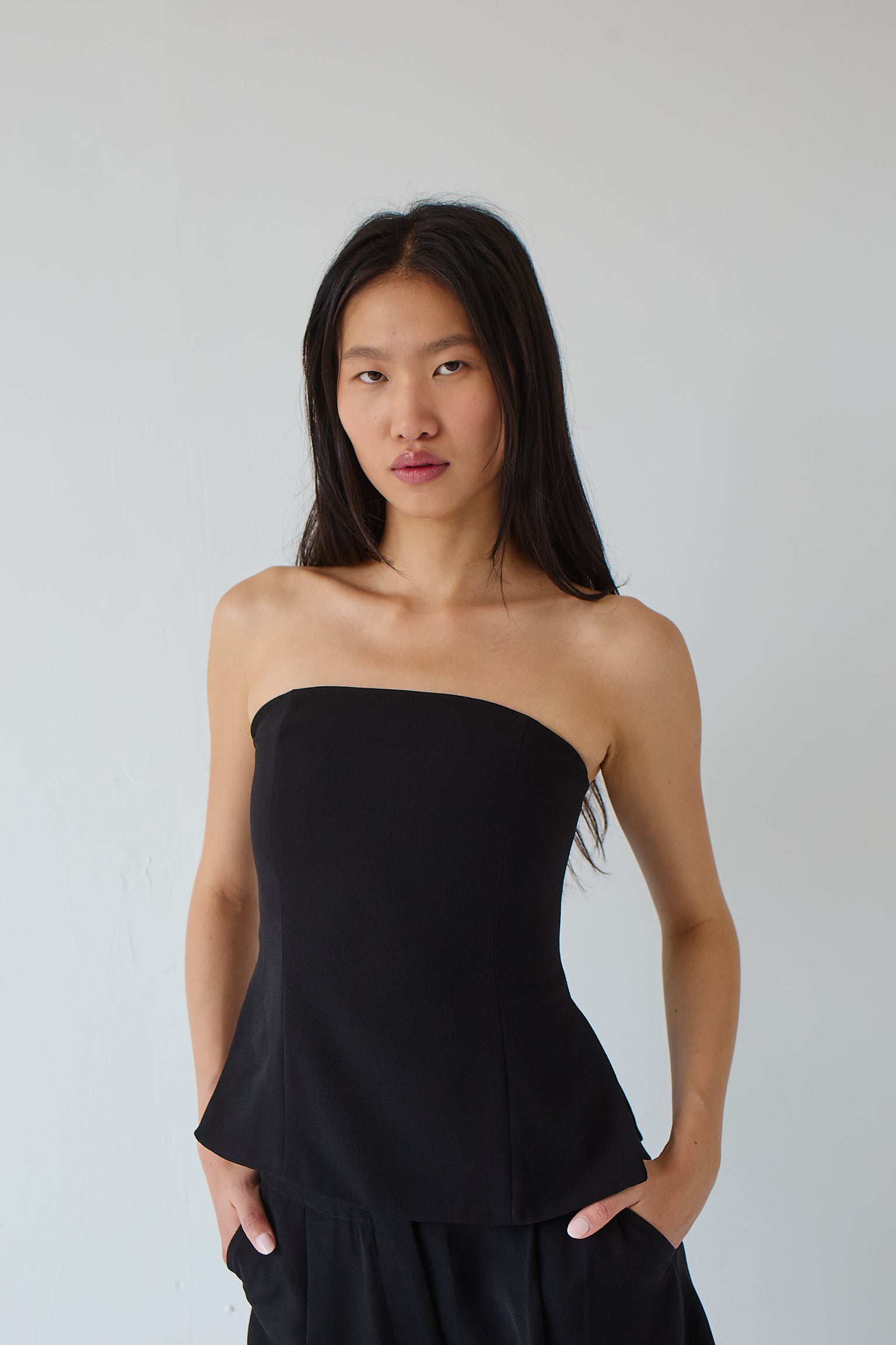 Woman wearing a black strapless top against a plain background