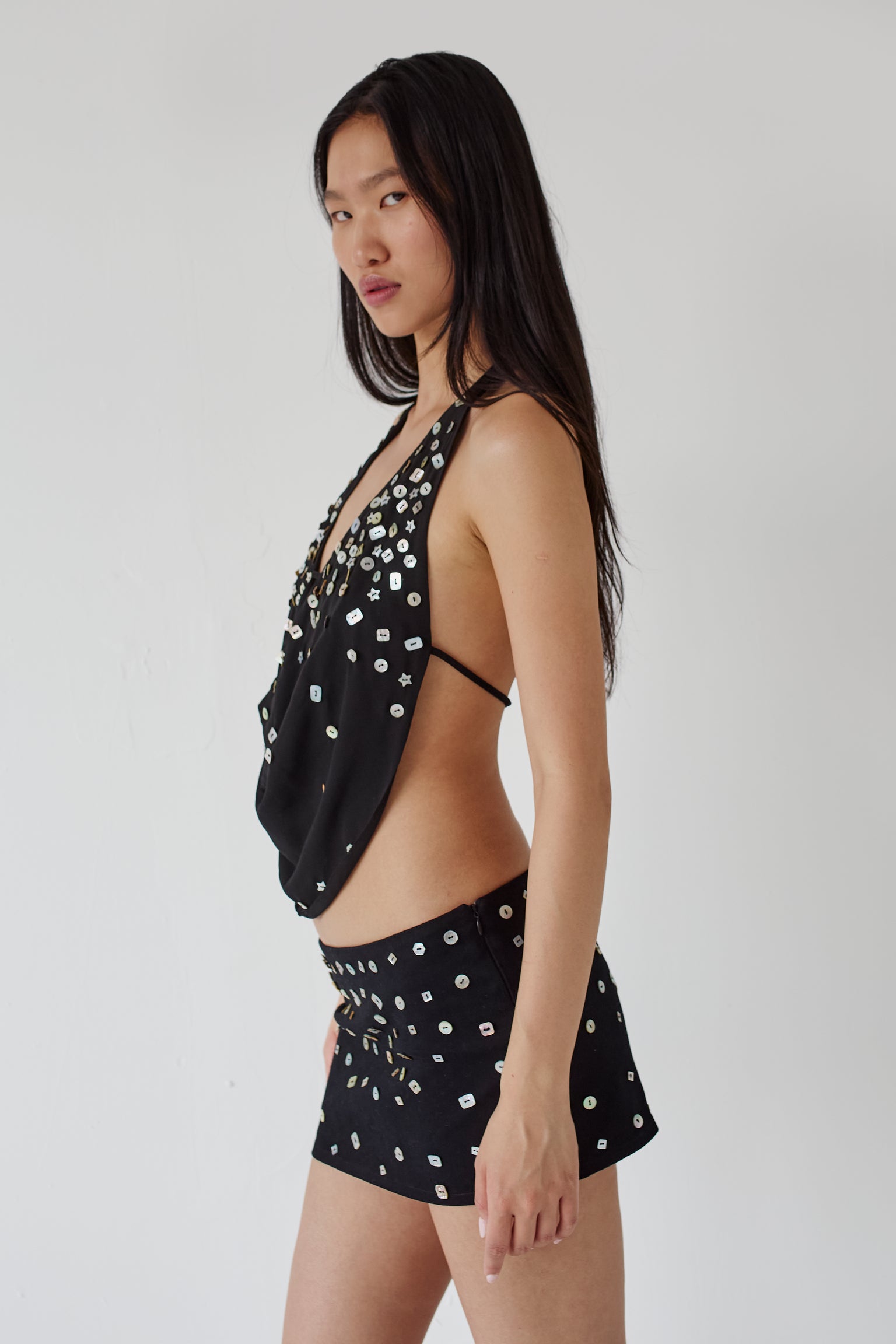 Woman wearing a black halter top with button embellishments and a matching mini skirt on a white background