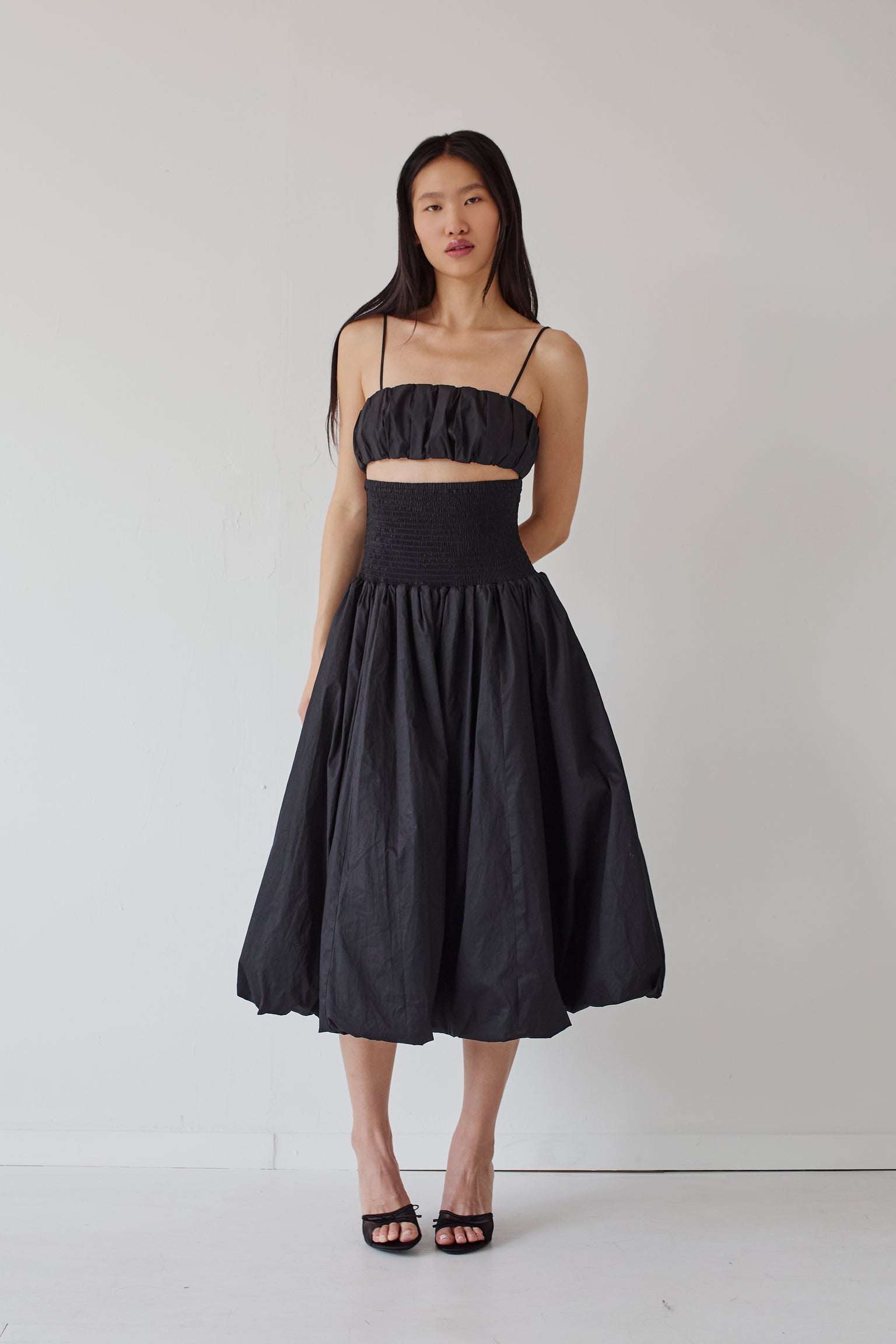 Woman wearing a black puffy bralette and a matching puffy skirt against a white background.