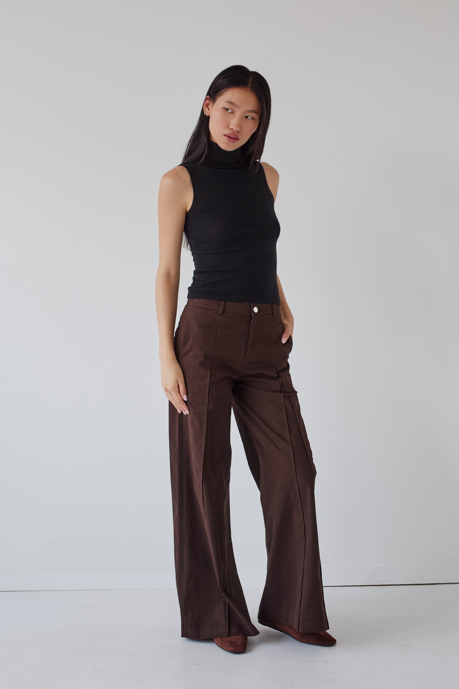 Woman wearing a black sleeveless top and brown wide-leg pants on a white background