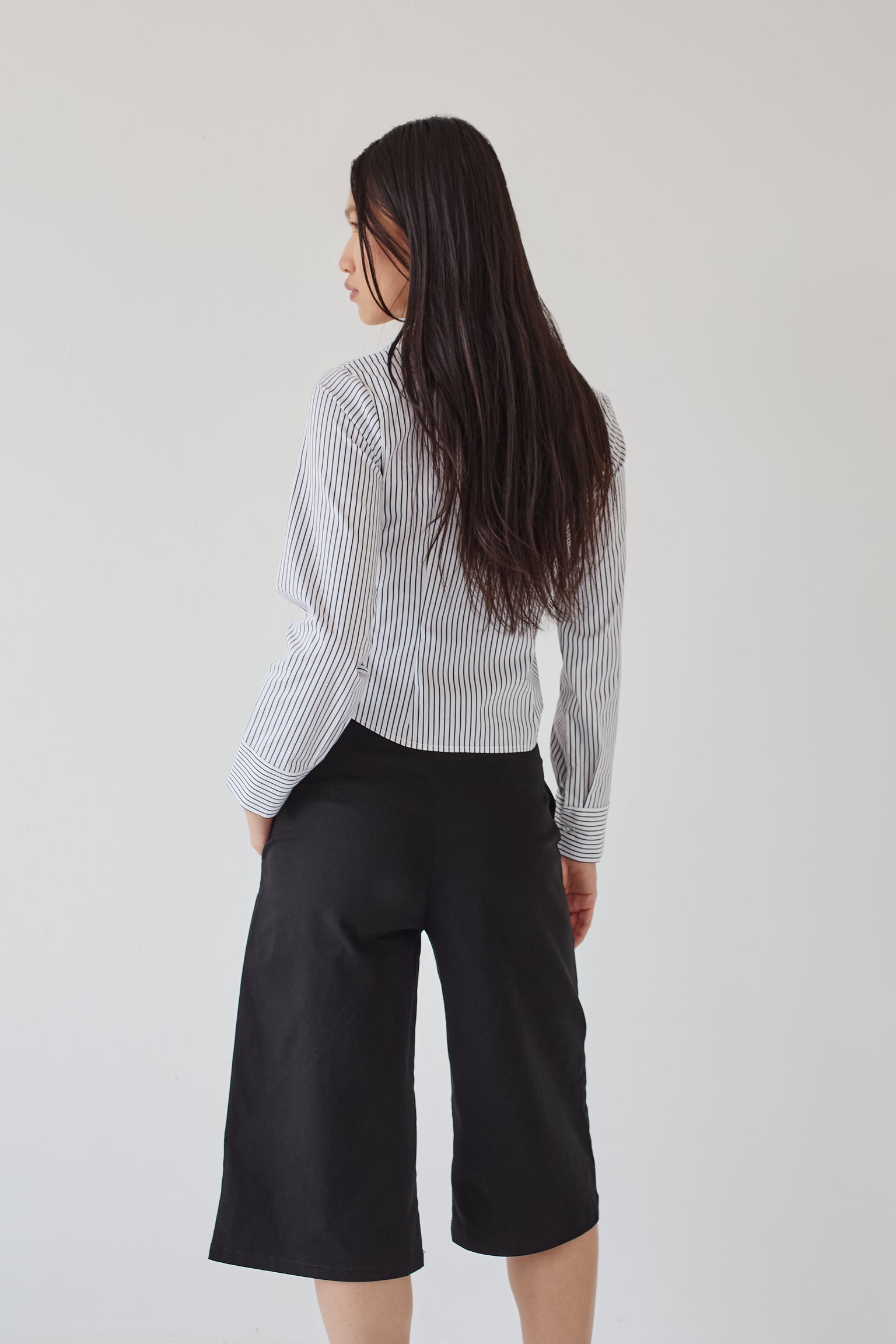 Woman wearing a striped shirt and black bermuda shorts on a plain background