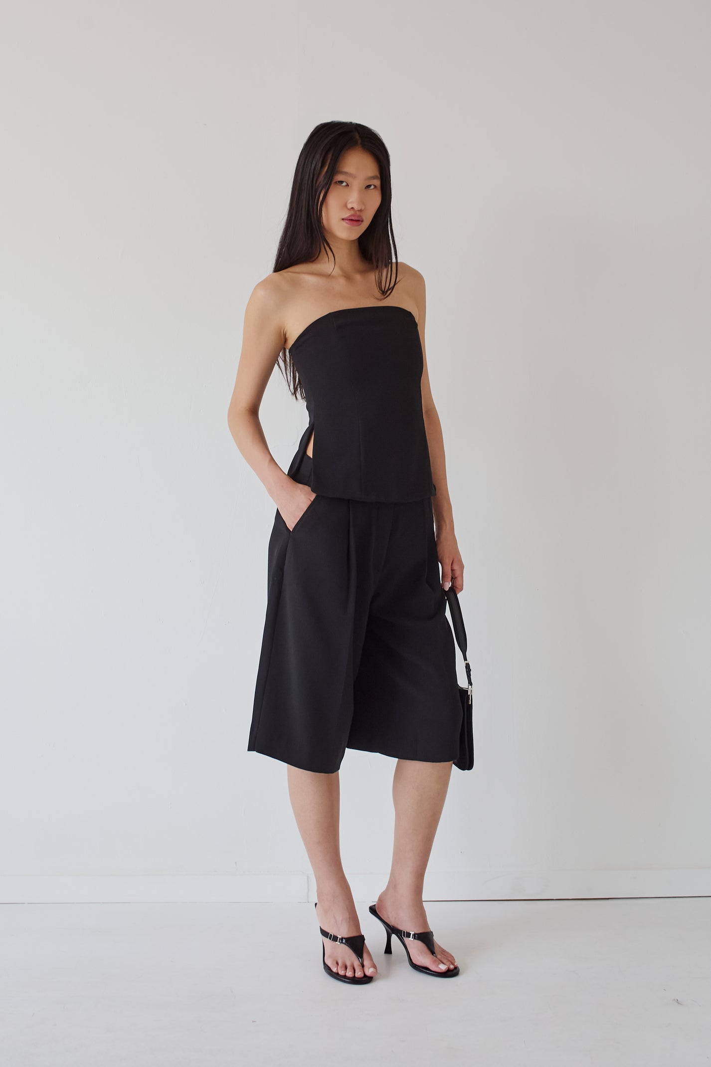 Woman wearing a black strapless top and wide-leg knee length pants against a white background