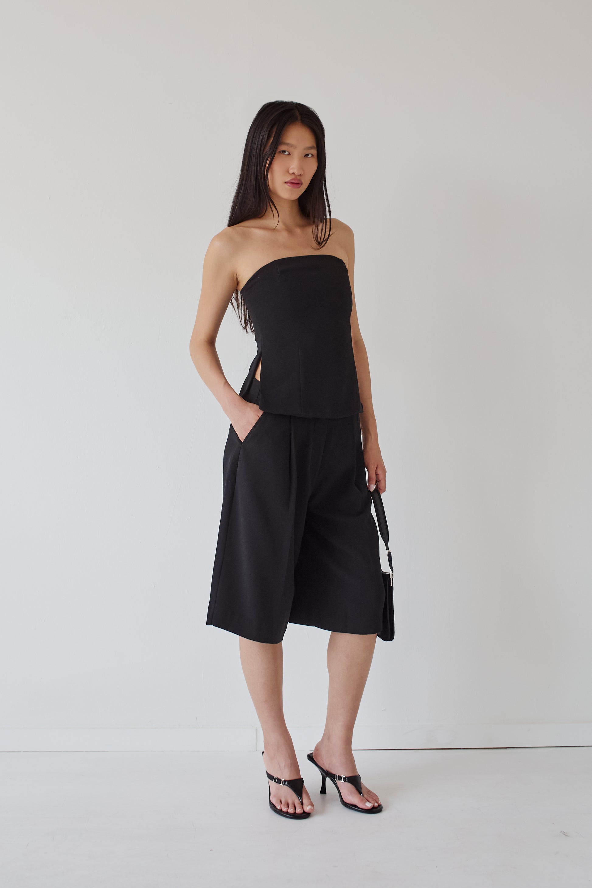 Woman wearing a black strapless top and wide-leg knee length pants against a white background