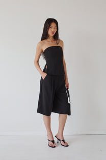 Woman wearing a black strapless top and wide-leg knee length pants against a white background