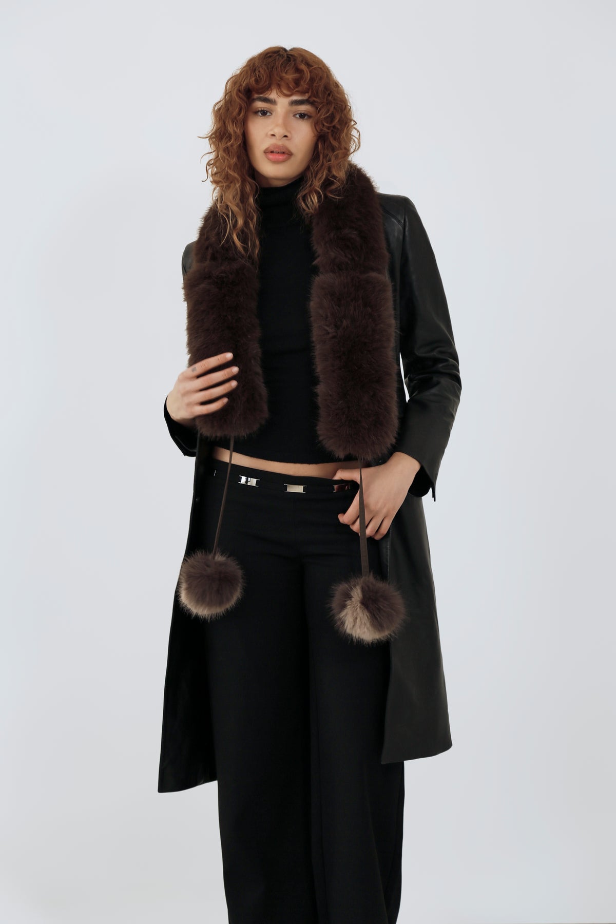 Model wearing an all black outfit and a brown fur scarf against a plain background