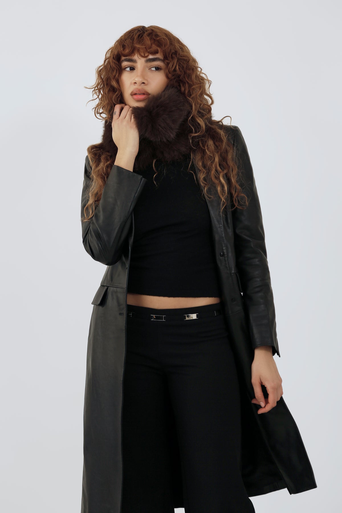 Model wearing an all black outfit and a brown fur scarf against a plain background