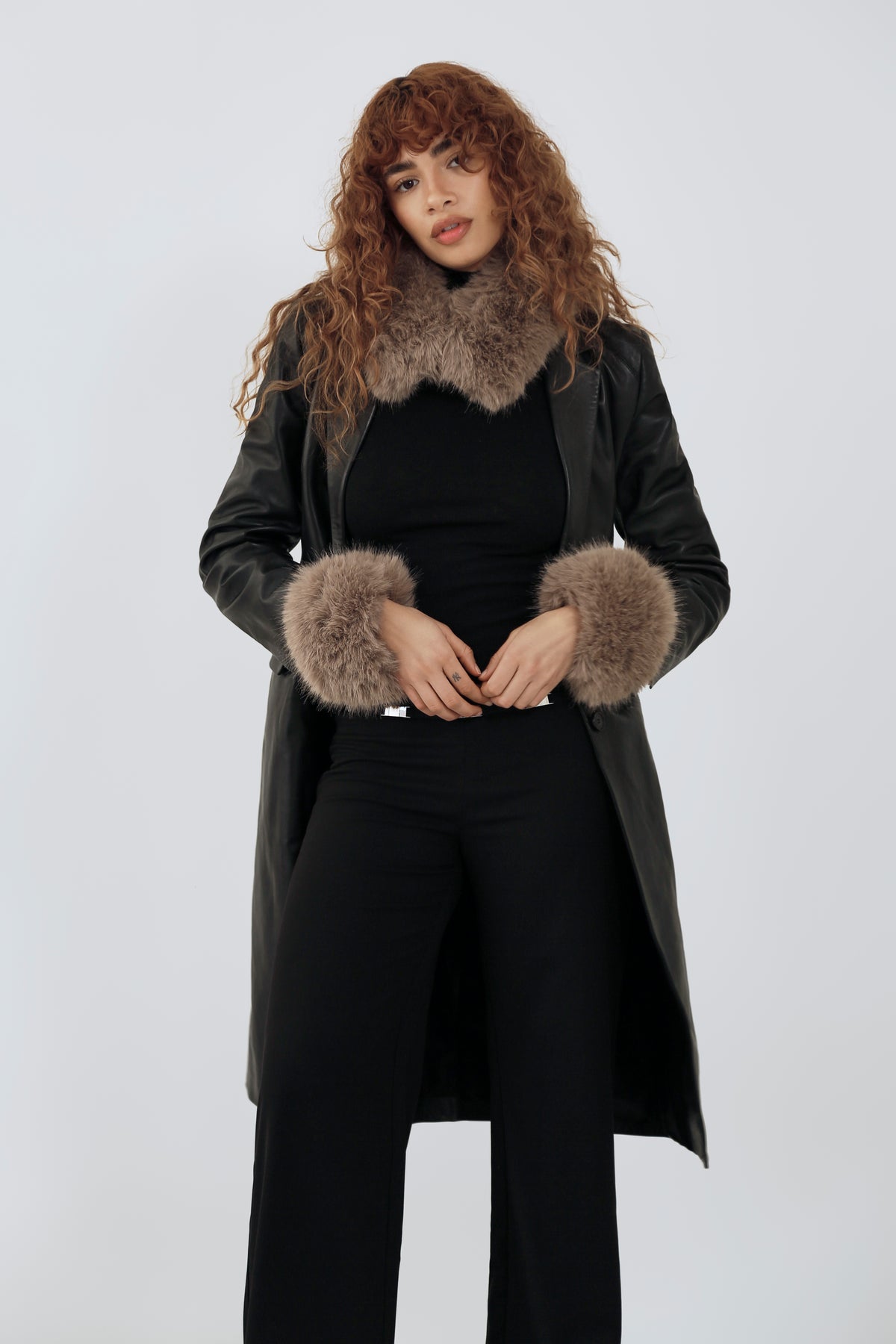 model wearing an all black outfit with a taupe fur scarf and cuffs against a plain background