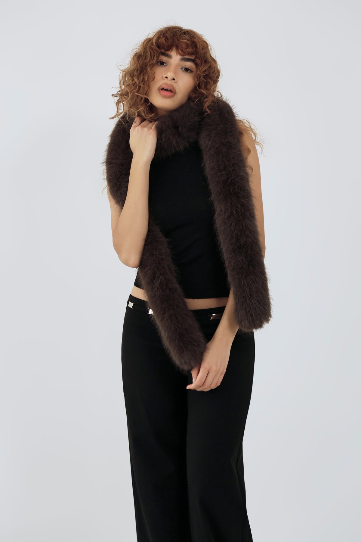 model wearing a black top and pants and brown furry scarf against a plain background