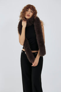 model wearing a black top and pants and brown furry scarf against a plain background