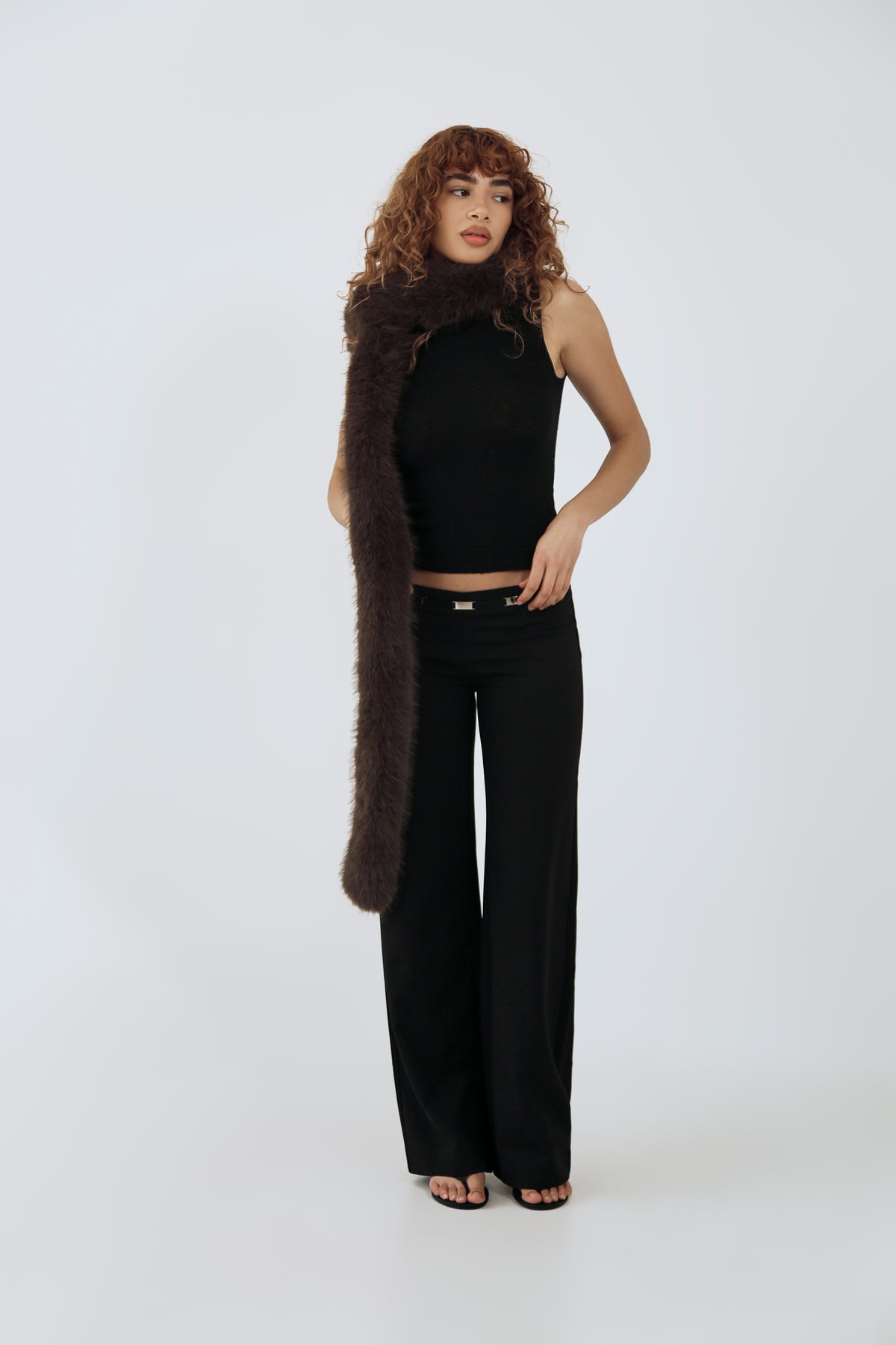 model wearing a black top and pants and brown furry scarf against a plain background