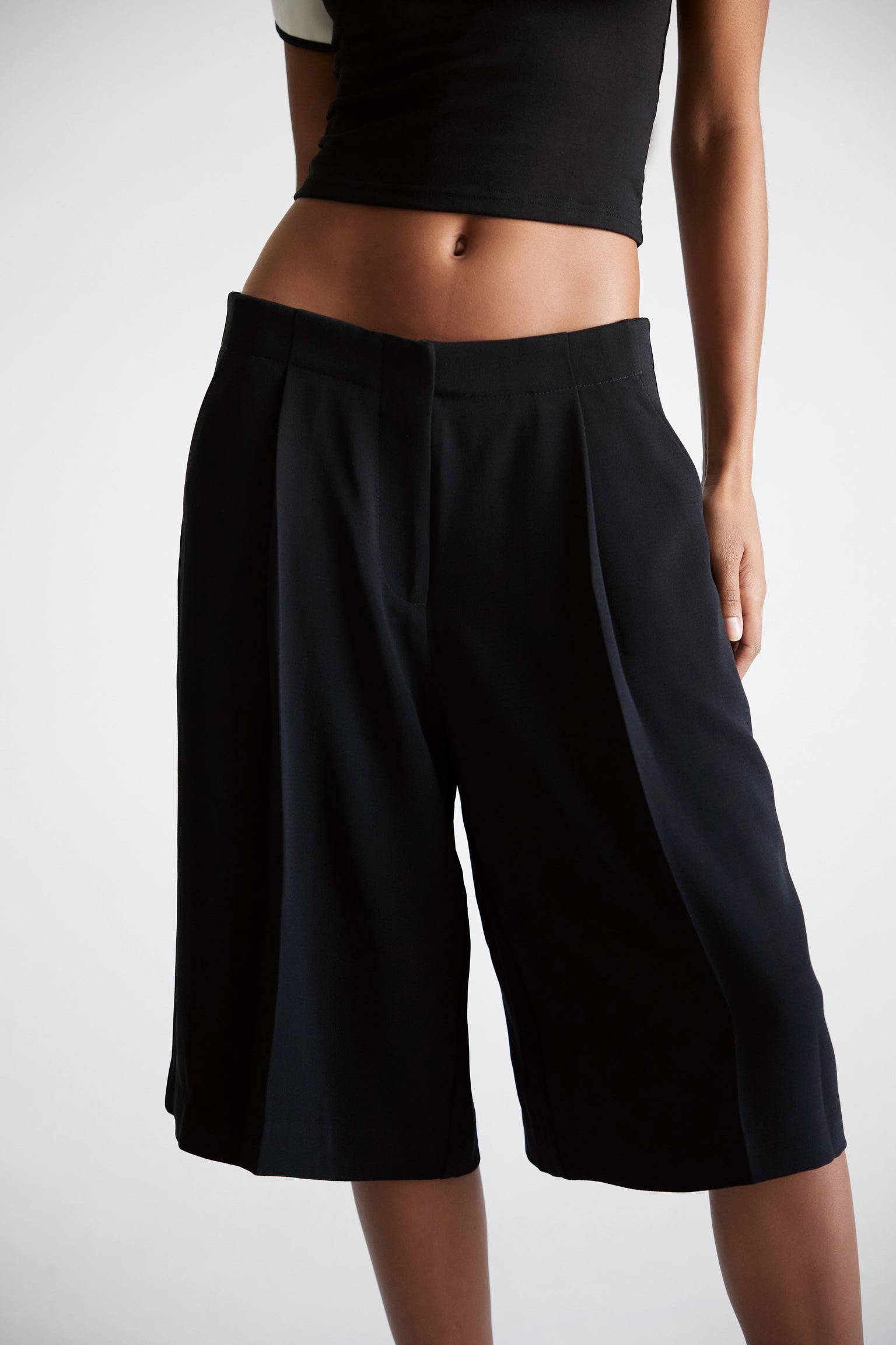 A closeup of a woman wearing black  tailored knee length shorts.