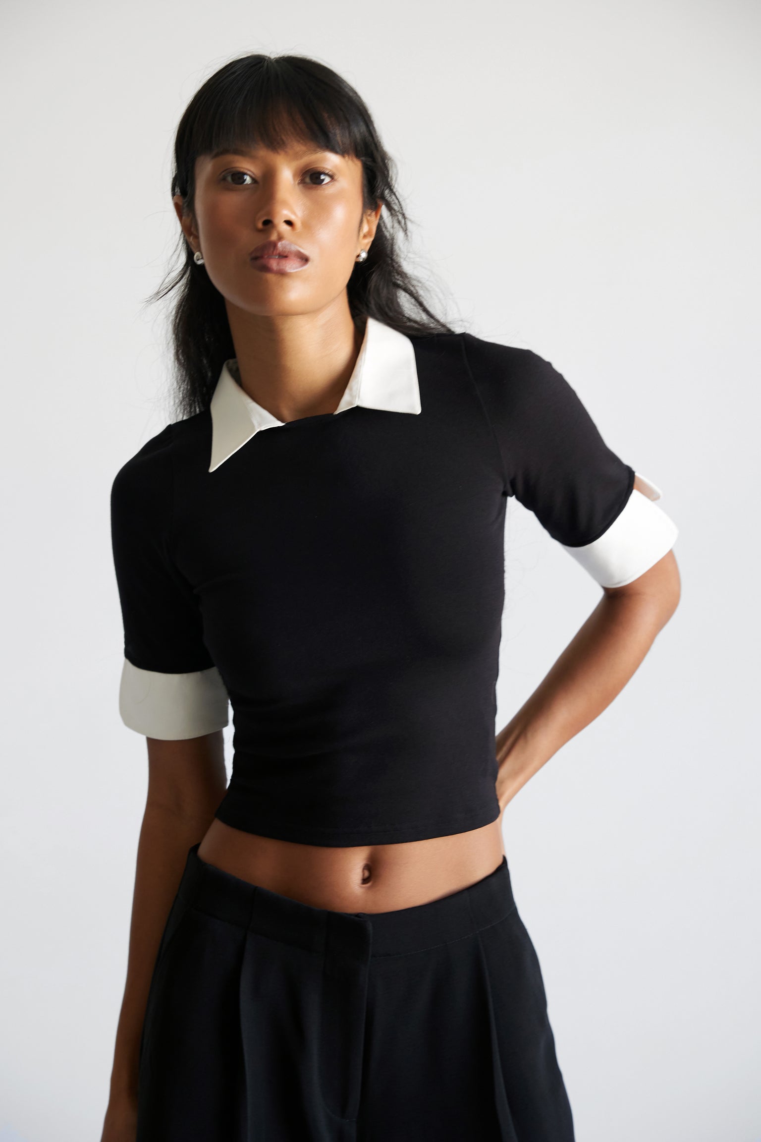 A woman wearing a black crop top with a contrasting white collar and white sleeve cuffs.