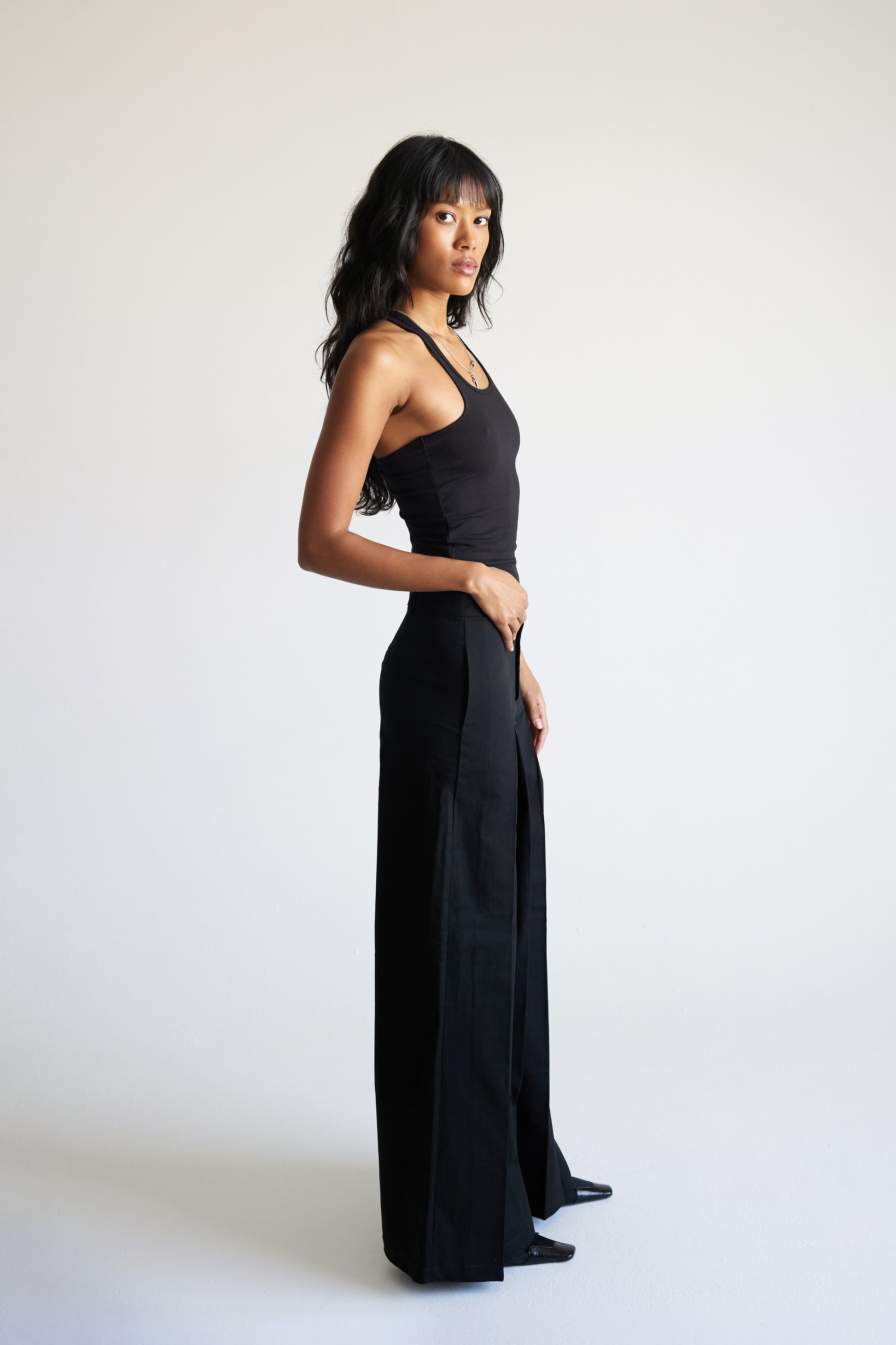 Woman wearing a black sleeveless top and wide-leg pants on a white background