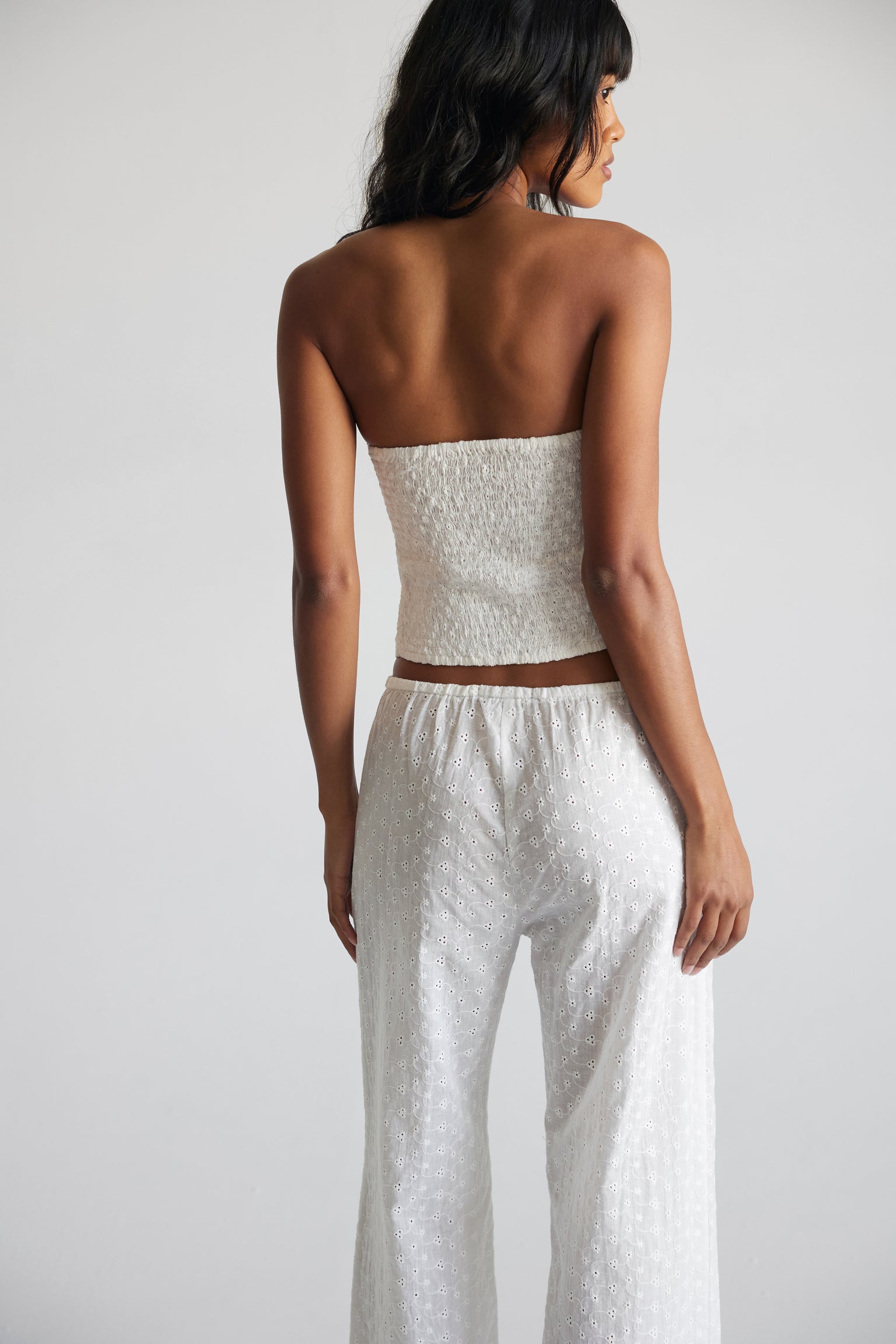 A woman wearing a white strapless top   paired with matching white pants against a neutral background.