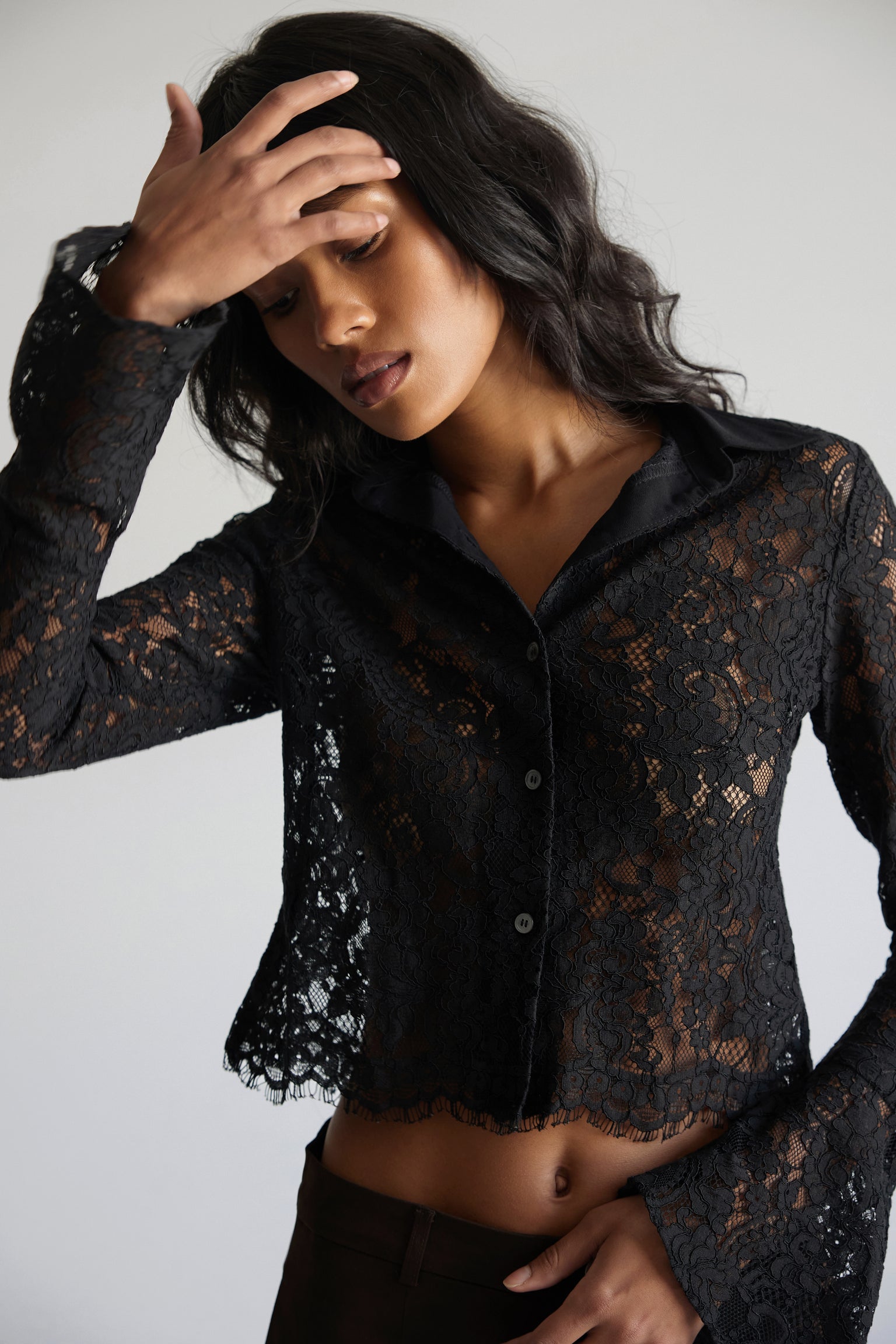 A woman wearing a black lace button-up blouse with bell sleeves and a solid crepe collar.