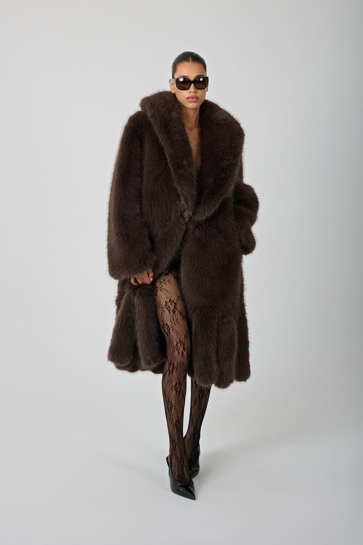 model wearing a brown fur coat and sunglasses against a blank background