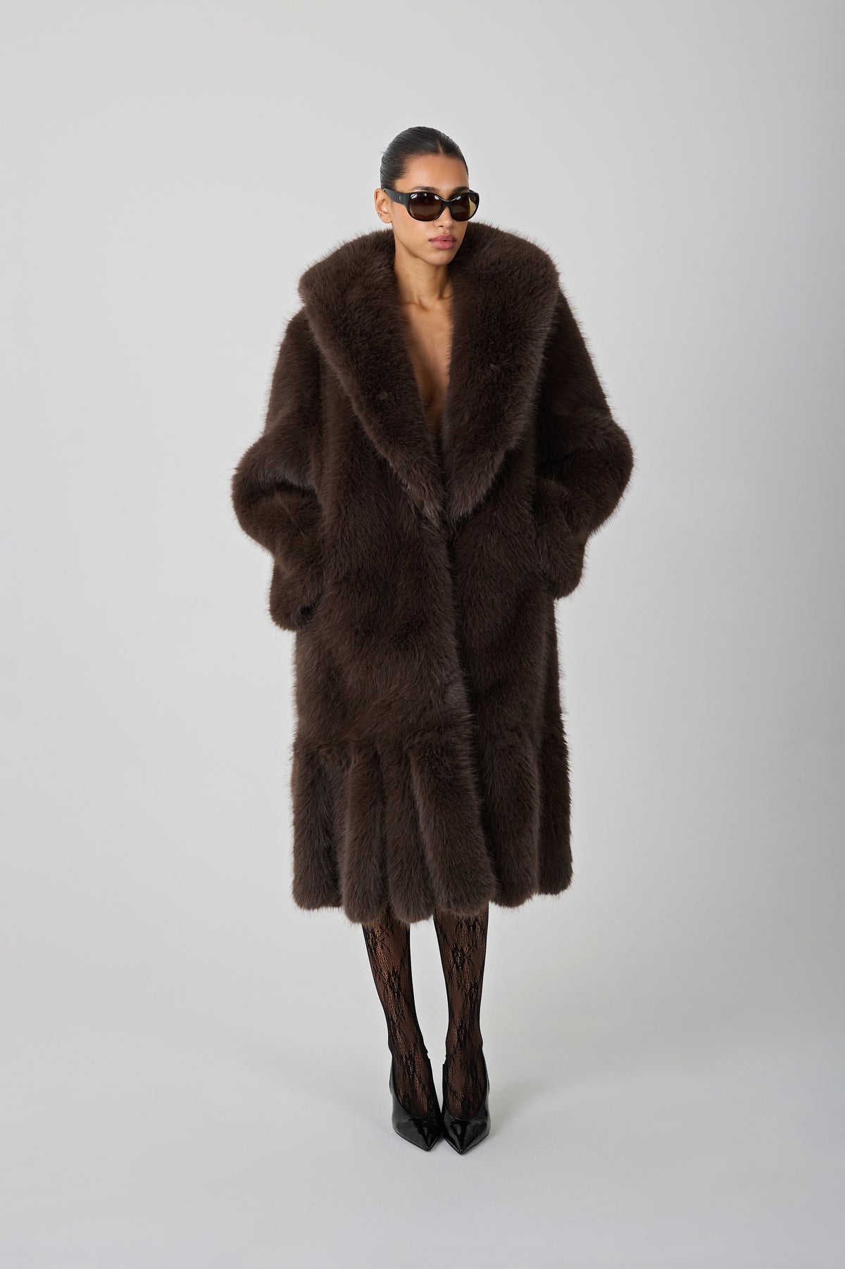 model wearing a brown fur coat and sunglasses against a blank background