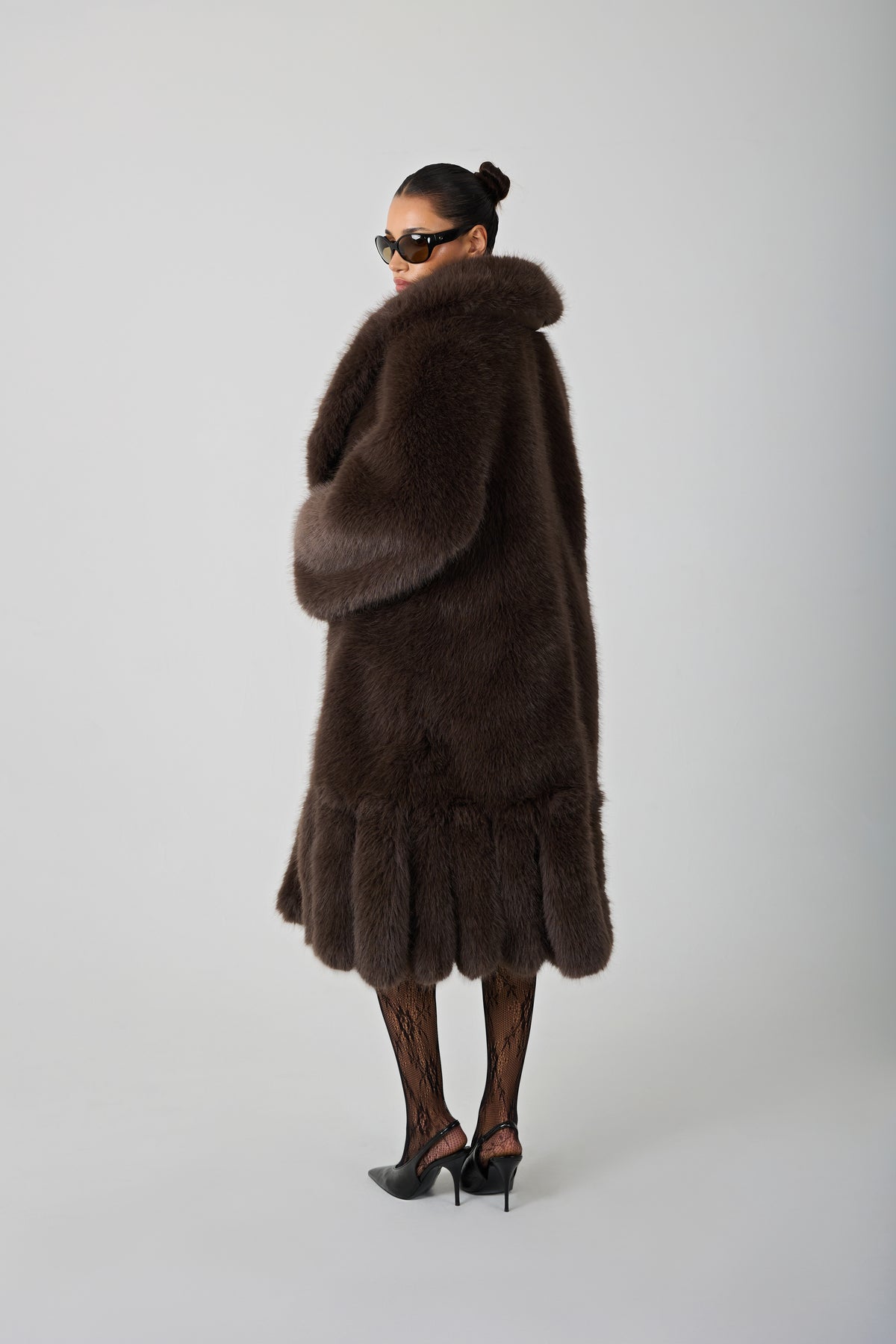 model wearing a brown fur coat and sunglasses against a blank background