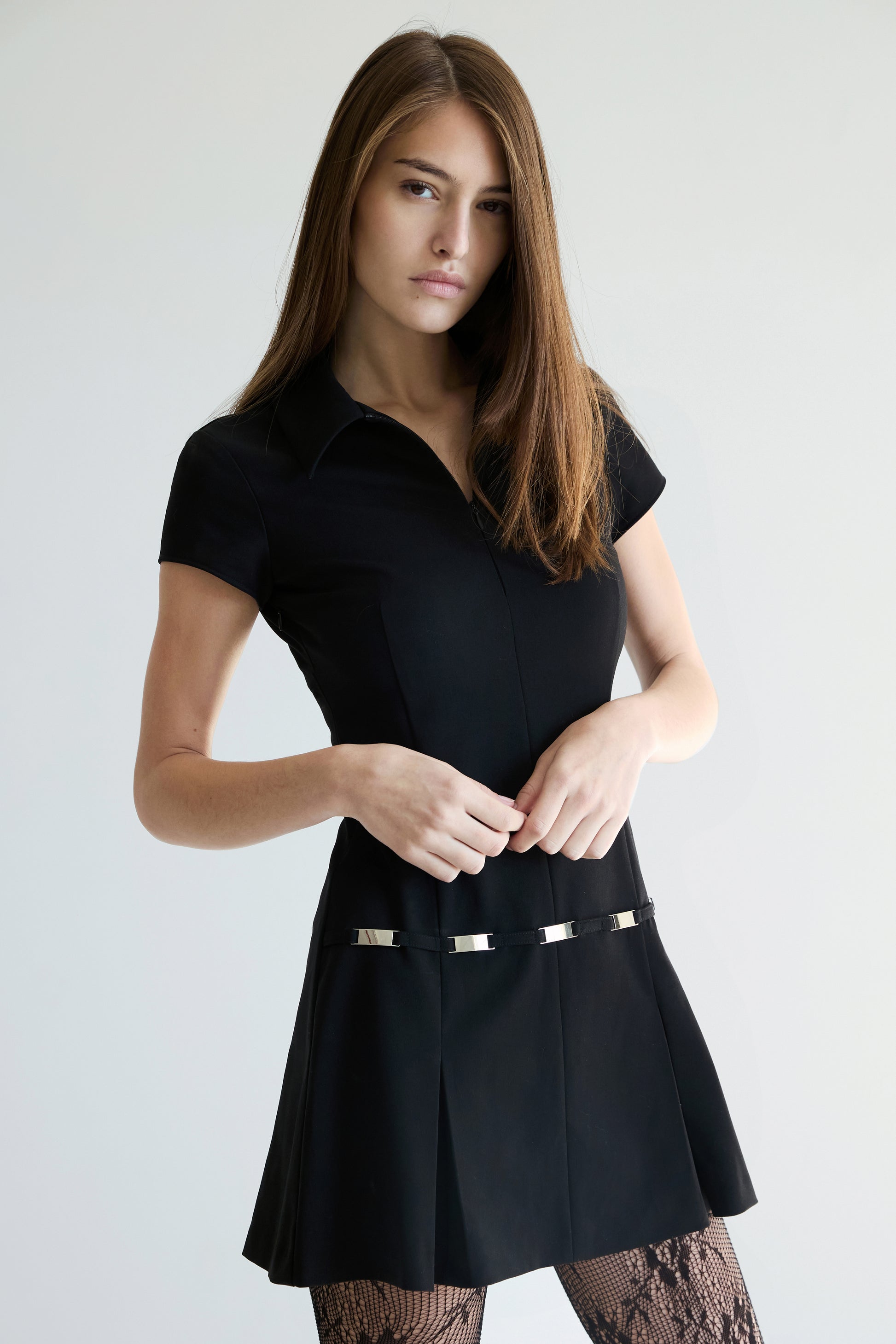 Woman wearing a black dress with a silver tone belt against a plain background