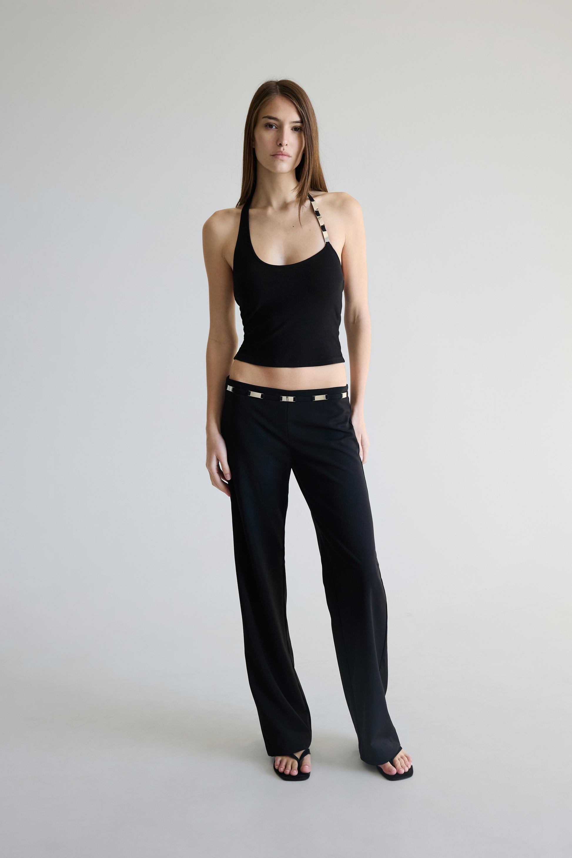 Woman wearing a black tank top and pants on a plain background