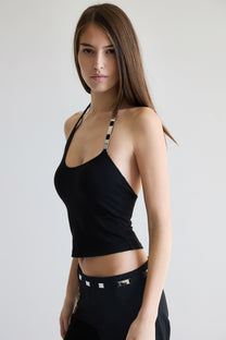 Woman wearing a black halter top and black pants with metal accents on a plain background