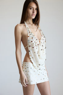 Woman wearing a cream halter top with silver embellishments and a matching skirt on a white background