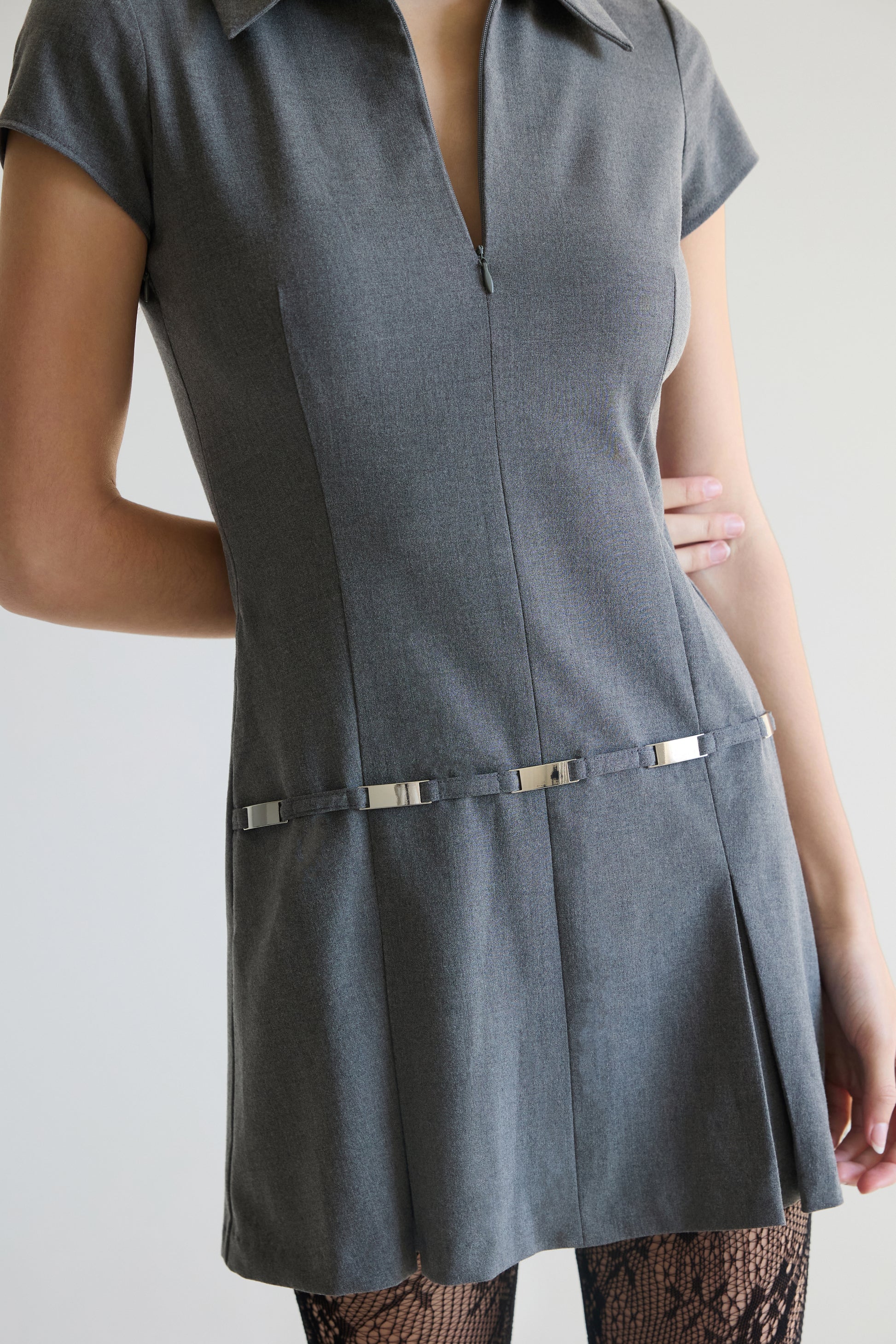 Woman wearing a gray dress with a zipper  and metal belt detail on a plain background