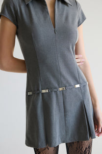 Woman wearing a gray dress with a zipper  and metal belt detail on a plain background