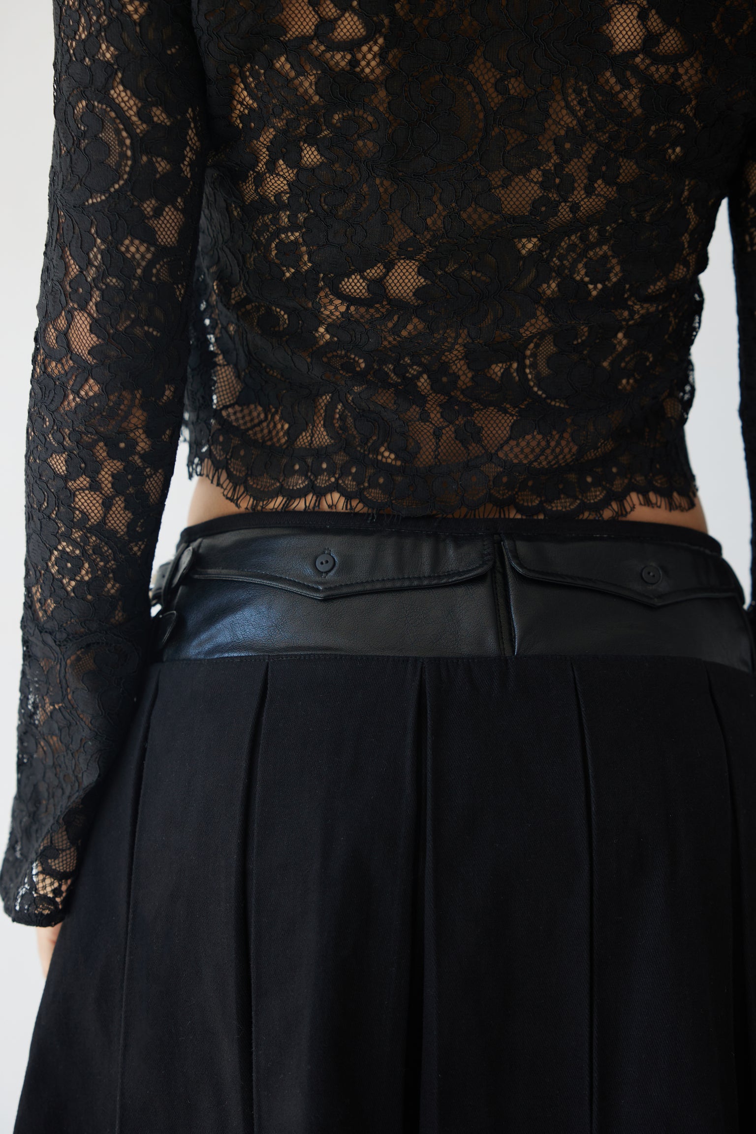 An up-close shot of a woman wearing a black lace blouse and a black pleated skirt with pocket details.