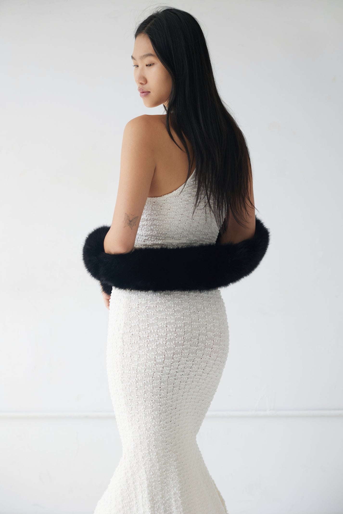 Woman wearing a white dress with a black fur scarf as a shrug against a white background