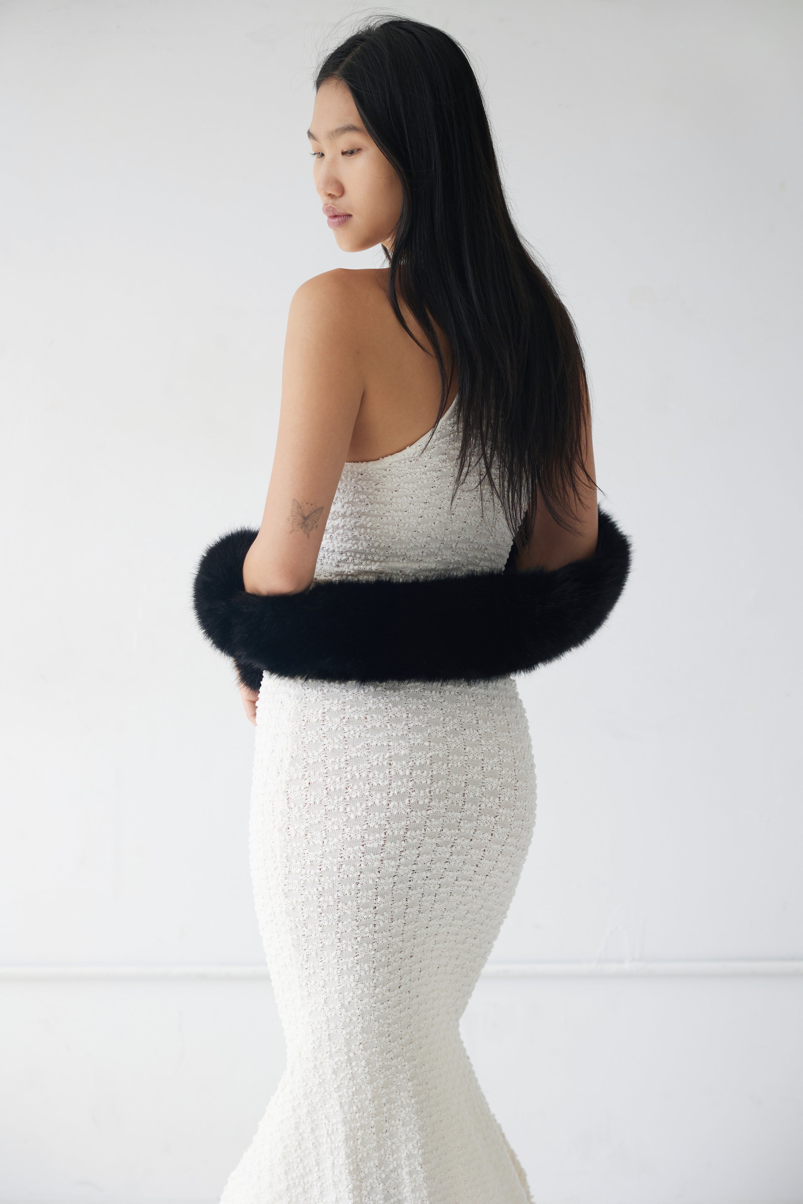 Woman wearing a white dress with a black fur scarf as a shrug against a white background