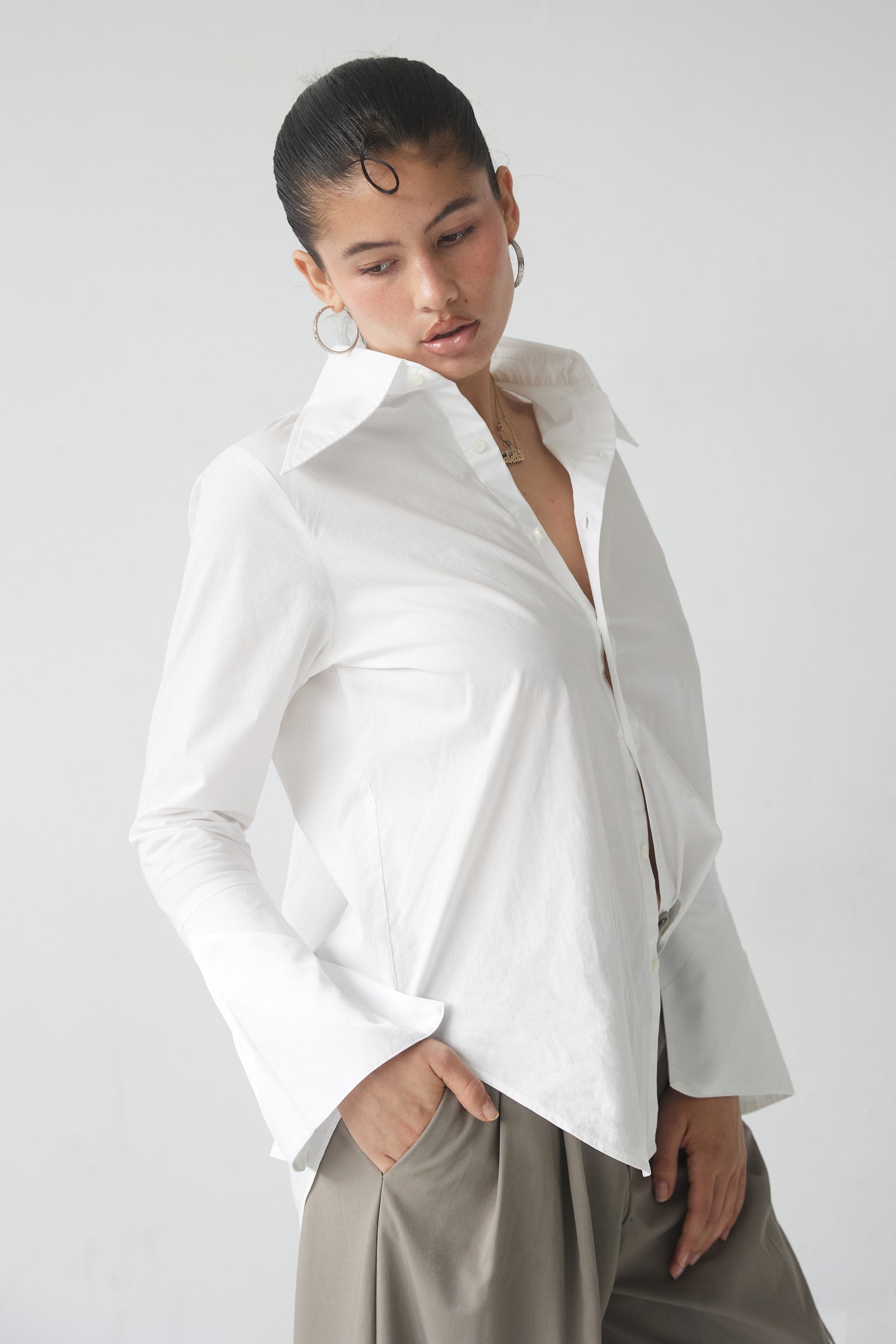 A woman wearing a white button-up shirt with an exaggerated collar and cuffs, standing against a neutral background.