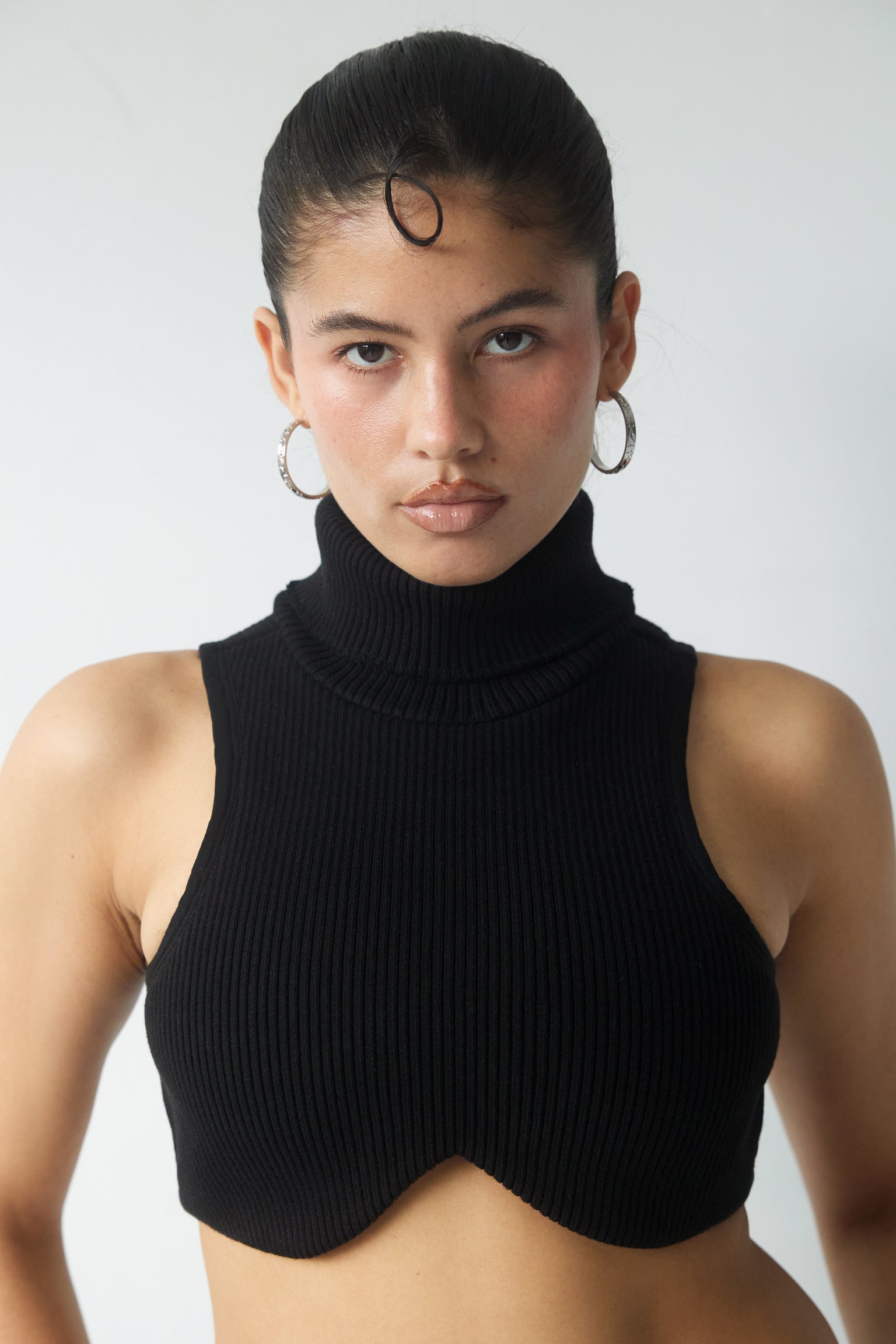 A woman wearing a black rib knit turtleneck top with underwire detail paired with silver tone hoops.