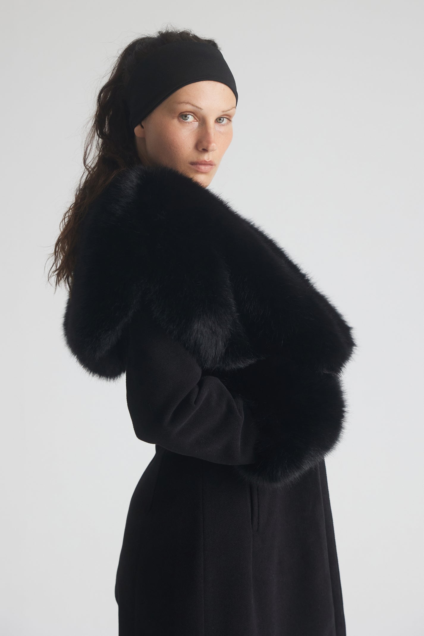Woman wearing a black coat with a fur collar against a white background